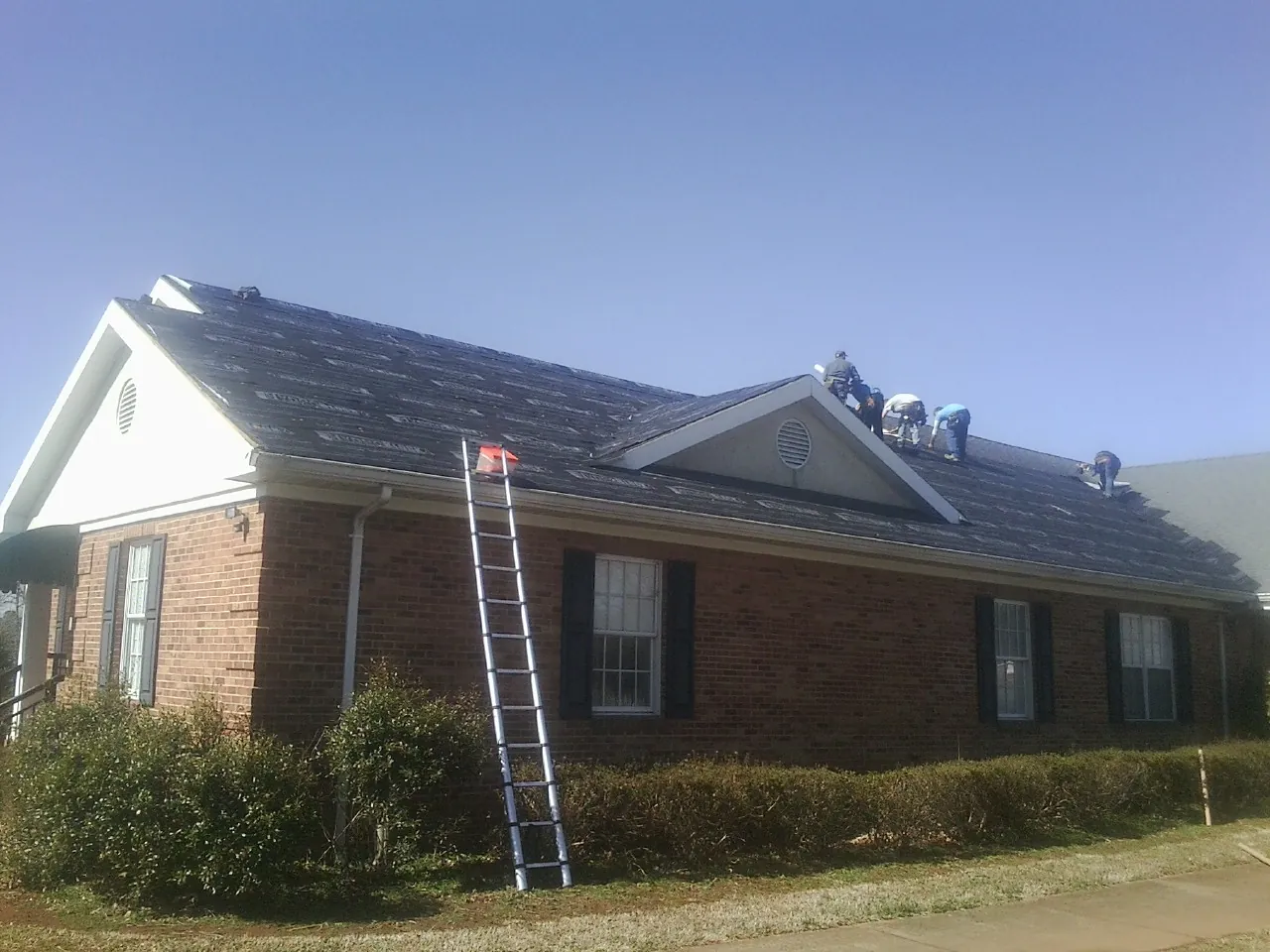 Crew tearing shingles off a brick ranch roof with a ladder set — Metal Roof Repair work by our crew in Gervais