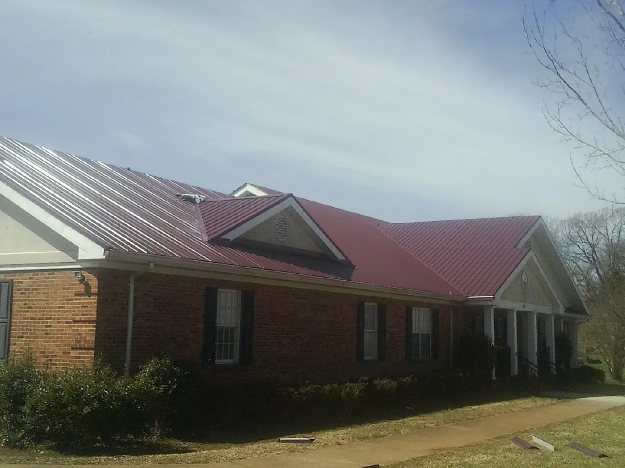 Red metal roof with gabled entries on a long brick building, from a Hail Damage Roof Repair job in Gervais