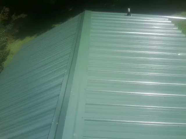 New green metal panels meeting at the ridge of a roof — Flat Roof Repair work by our crew in Gervais