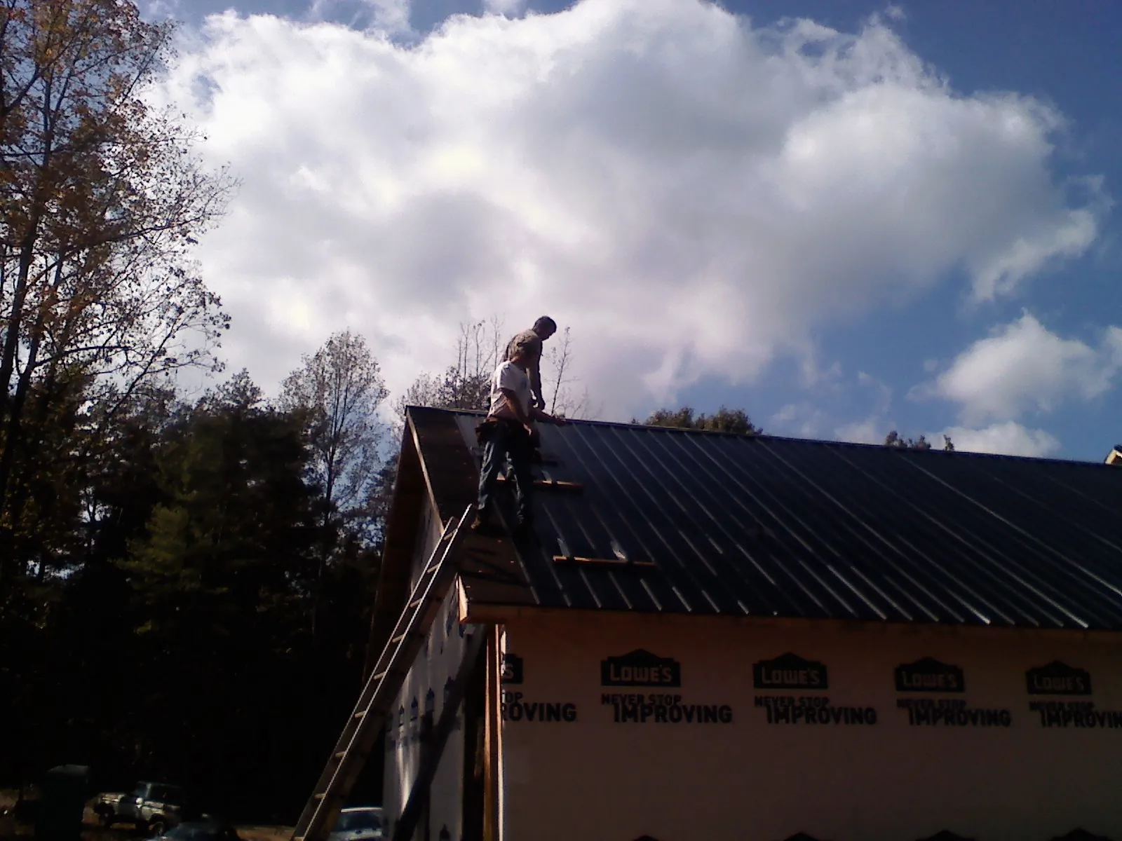 Roofer fastening dark metal panels high against a cloudy sky, from a Roof Inspection job in Gervais