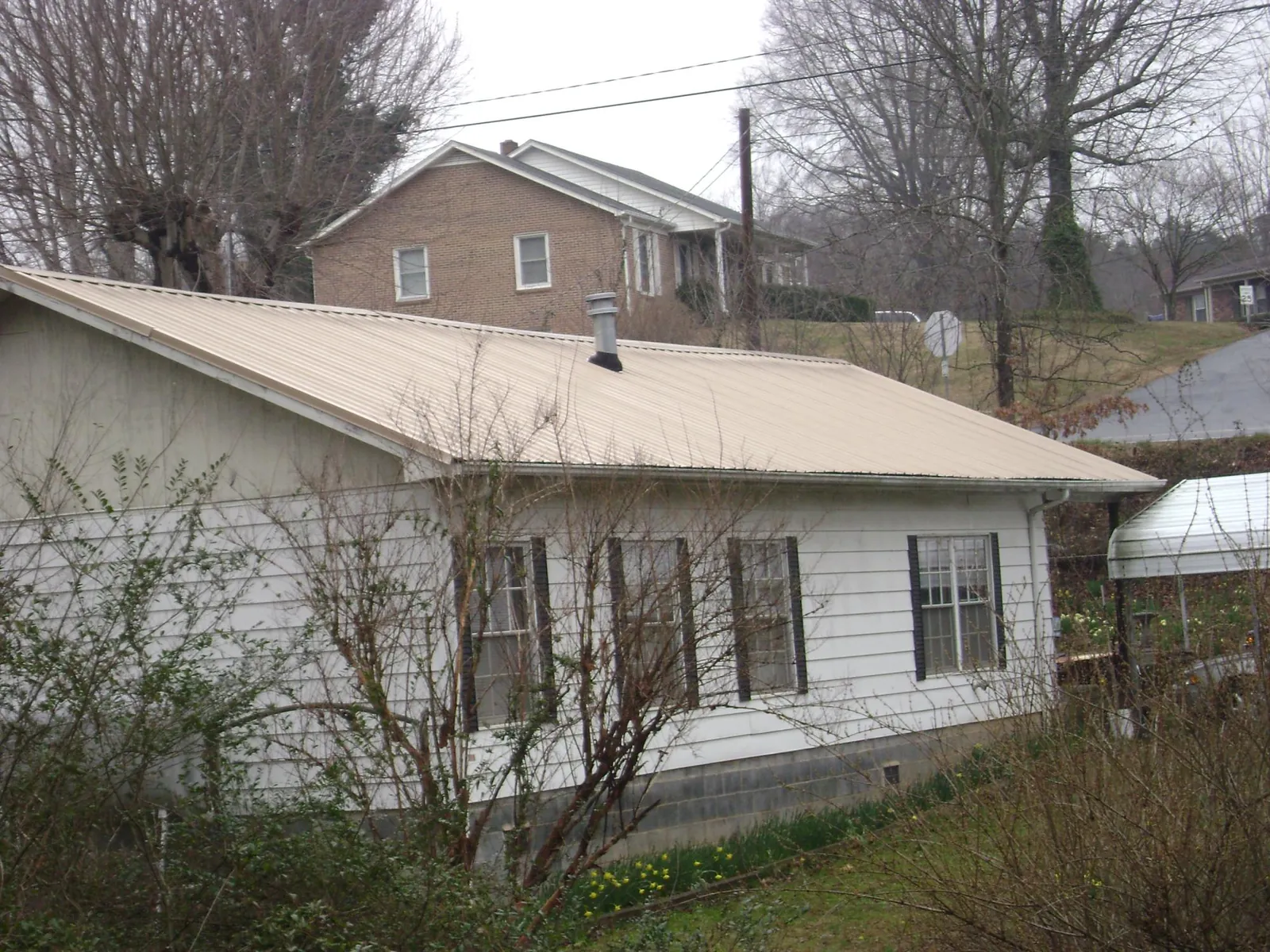 Tan metal roof on a white sided house set into a hillside — Commercial Roofing by Roofing Brothers in Gervais